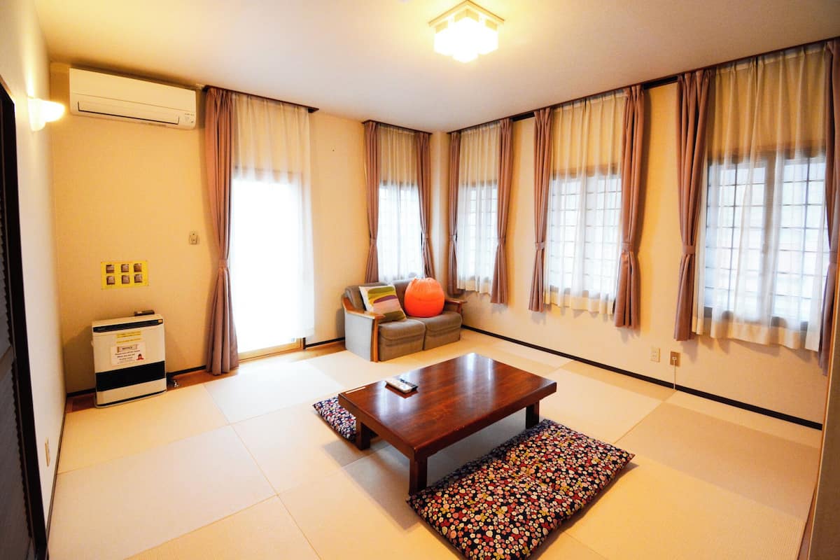 A spacious room with tatami flooring, a wooden table, a sofa, and a futon.