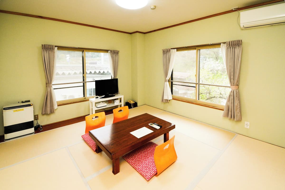 A room with tatami flooring, a wooden table with chairs, a television, and an air conditioning unit.