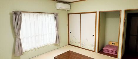 A room with tatami flooring, a wooden table, a window with curtains, a sliding door with a floral design, and an air conditioning unit.