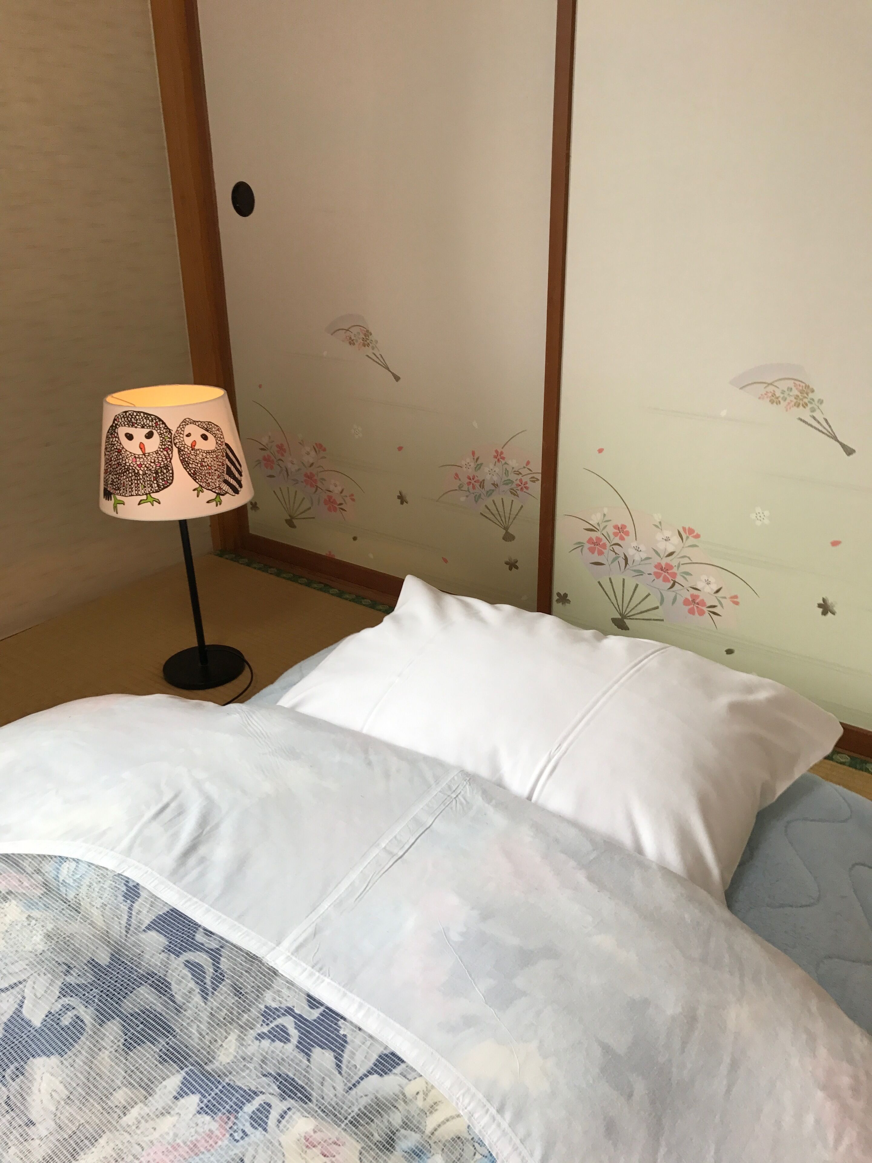 Habitación de hotel con cama, lámpara y un muro decorado con motivos florales y de aves.