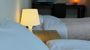 A hotel room with a bed, a bedside table with a lamp, a television, and a nightstand. - Belle Vue Nishiura (Minamiuonuma)