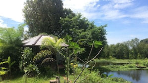 A rustic house with a tiled roof, surrounded by lush greenery and a calm pond.