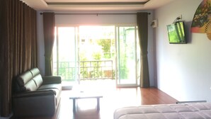 A room with a sofa, a bed, a table, and a view of the outdoors through a sliding door.