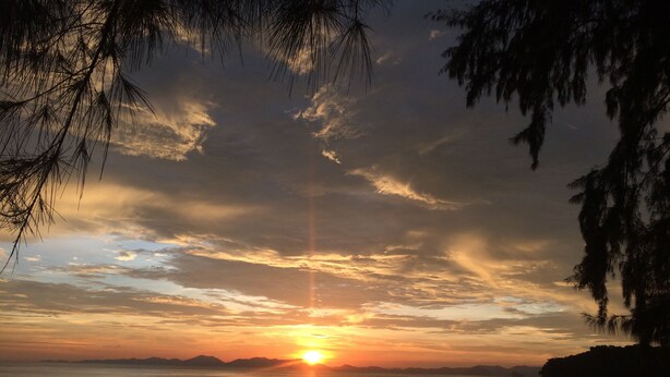 A beach with a sunset, trees, and mountains in the distance.