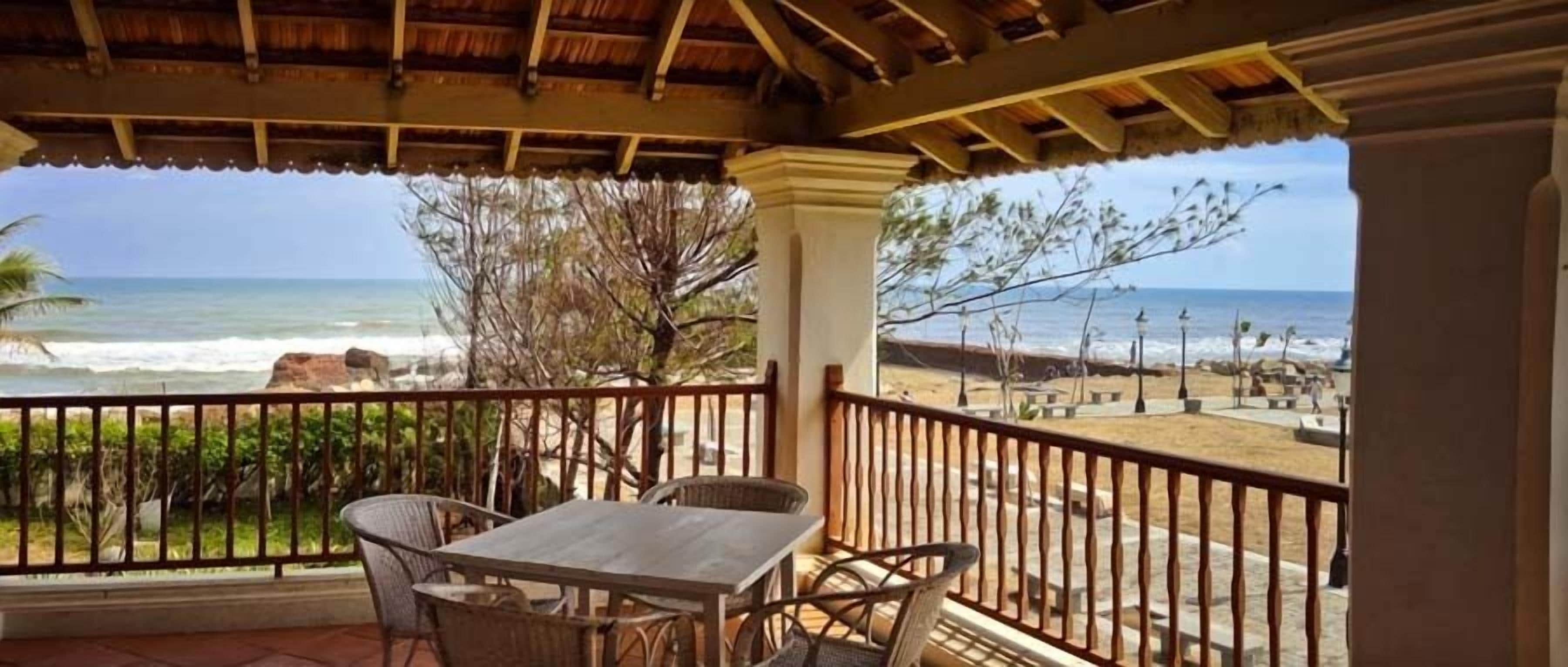 Ein überdachter Außenbereich mit Tisch und Stühlen mit Blick auf Strand und Meer.