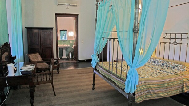 Una habitación tradicional con cama con dosel, un escritorio de madera, una silla y un armario.
