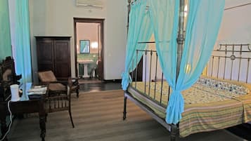 A traditional room with a four-poster bed, a wooden desk, a chair, and a wardrobe.