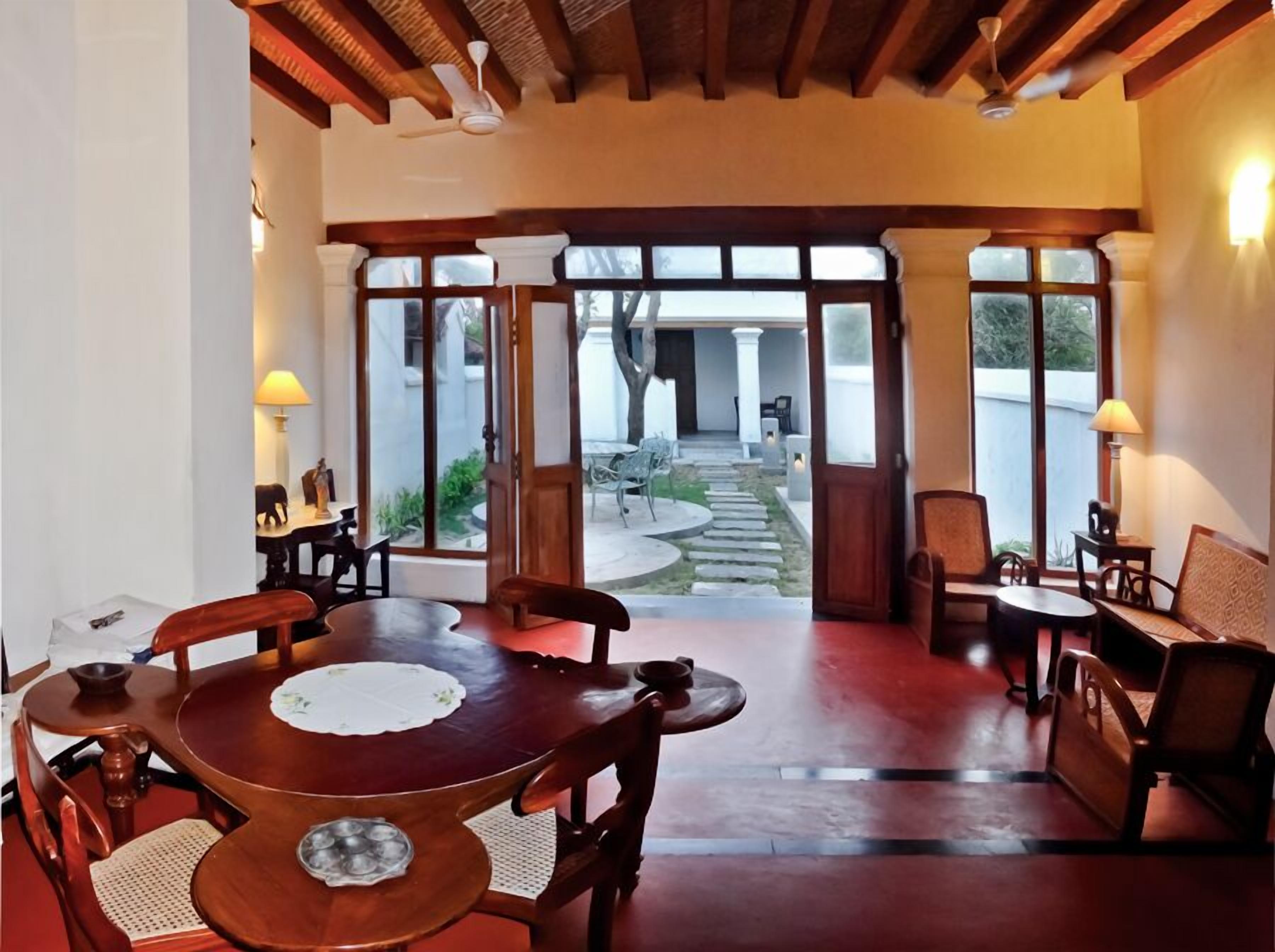 Un comedor con una mesa y sillas de madera, vista al patio exterior a través de puertas de vidrio y un ventilador de techo.