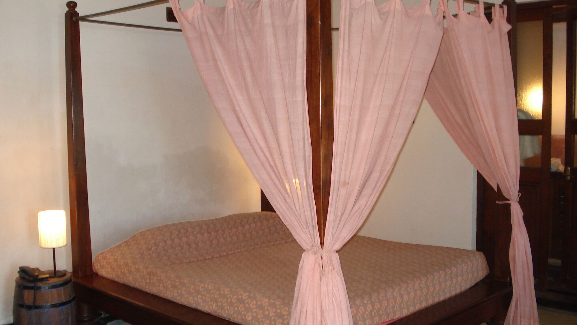 Una cama con dosel decorada con un colchón estampado de flores y cortinas rosadas.