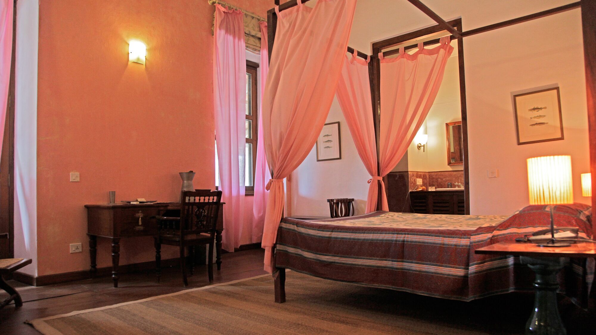 A bedroom with a four-poster bed, a desk, and a chair.