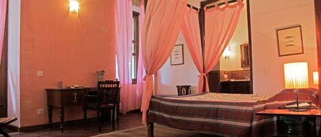 A bedroom with a four-poster bed, a desk, and a chair.