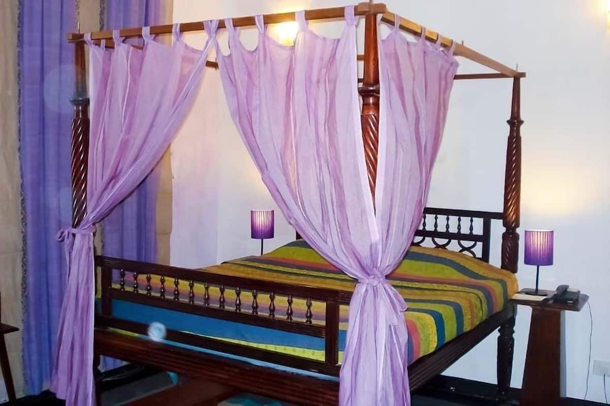 Una cama con dosel adornada con una colcha a rayas de colores, cortinas moradas y dos lámparas de noche.