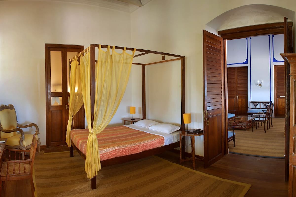 Una cama con dosel y mosquitera, un área de comedor con mobiliario de madera y una habitación separada con vistas.