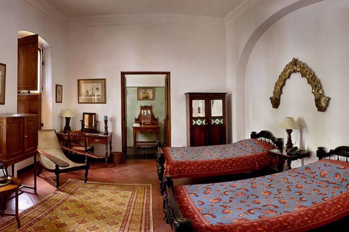 Una habitación con dos camas, un armario de madera, una silla, una mesa y un espejo.