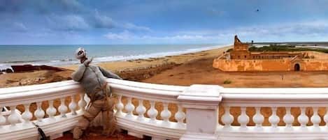 Vista costera con una fortaleza histórica y una persona apoyada en una barandilla blanca.