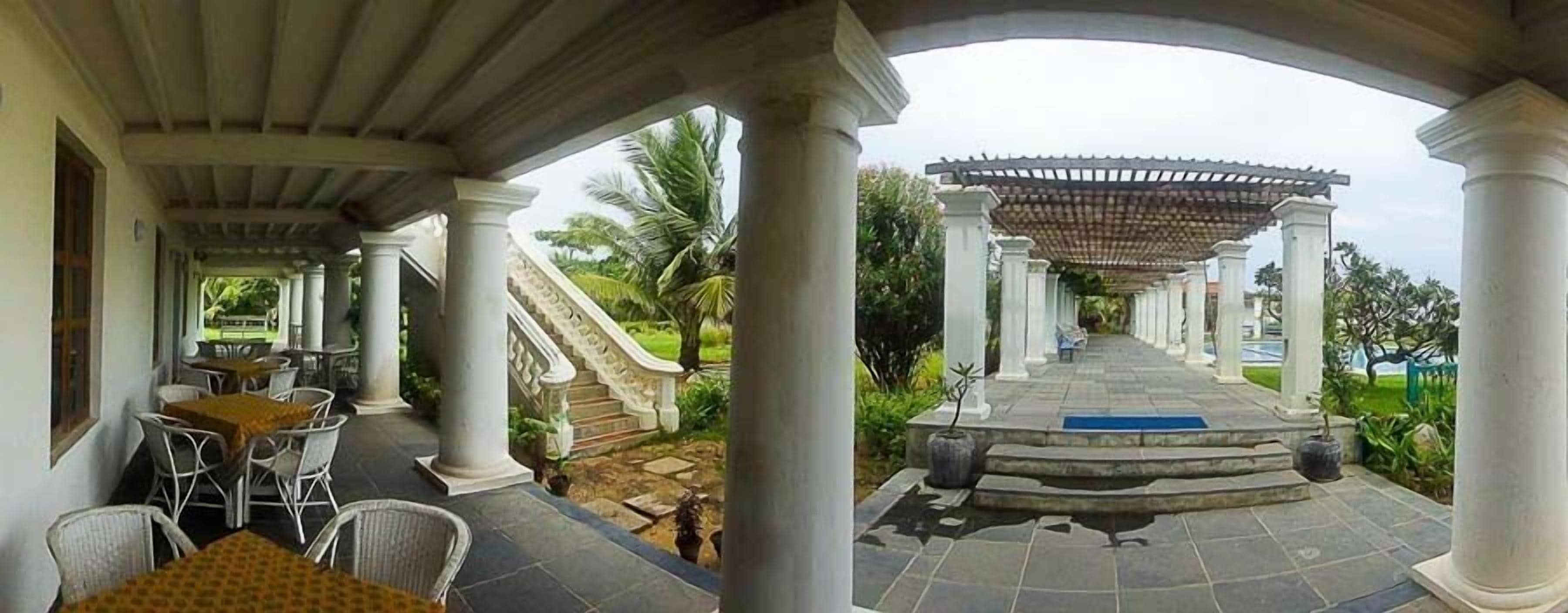 A covered outdoor area with white columns, a staircase, and tables with chairs.