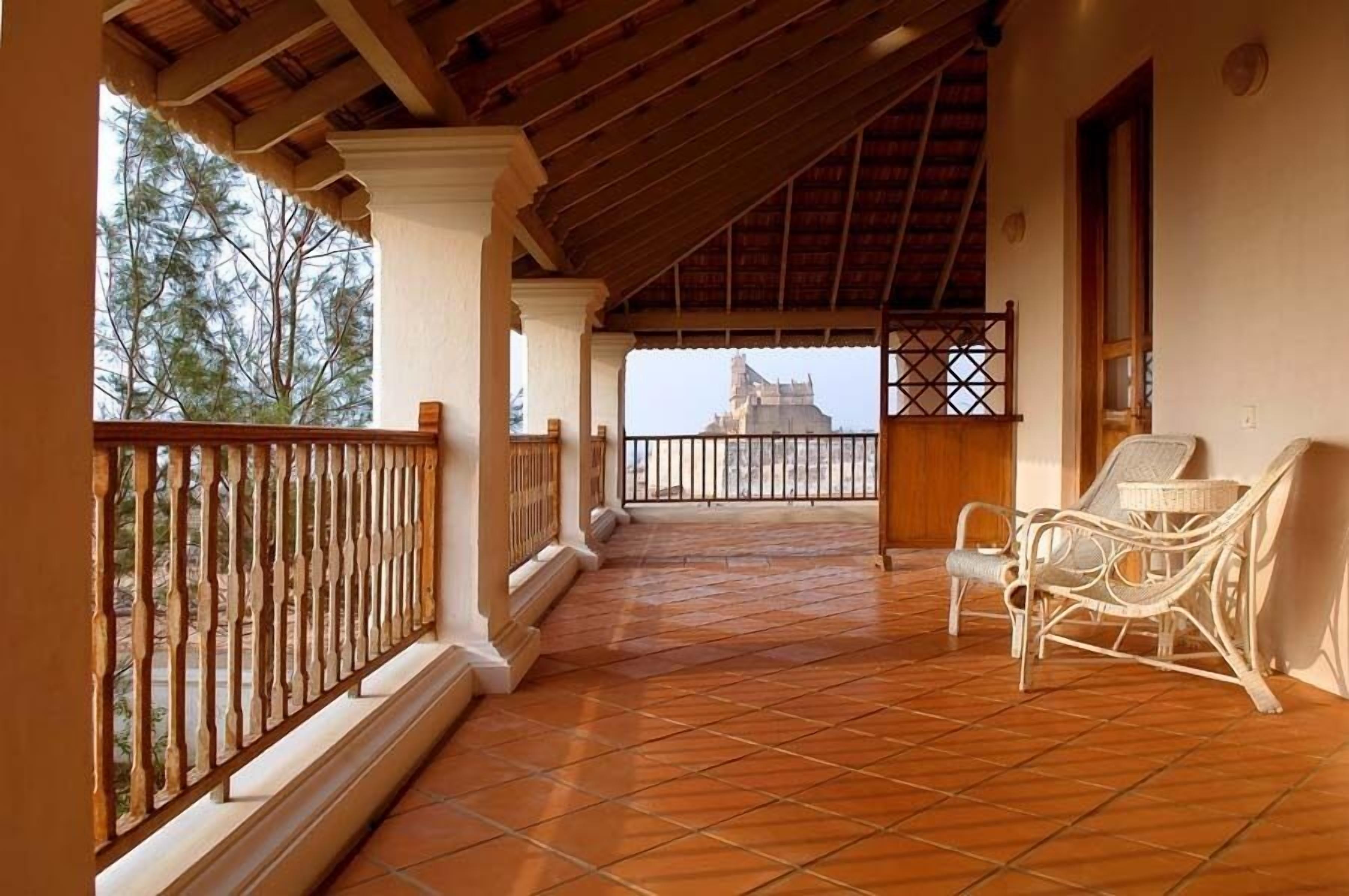 A covered balcony with tiled flooring, a wicker chair, and a view of a distant building.