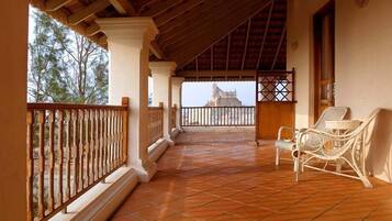 A covered balcony with tiled flooring, a wicker chair, and a view of a distant building.