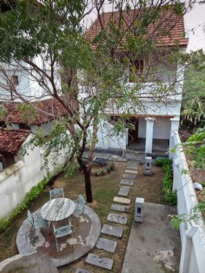 Un patio con un sendero de piedra, una mesa redonda con sillas y un árbol.
