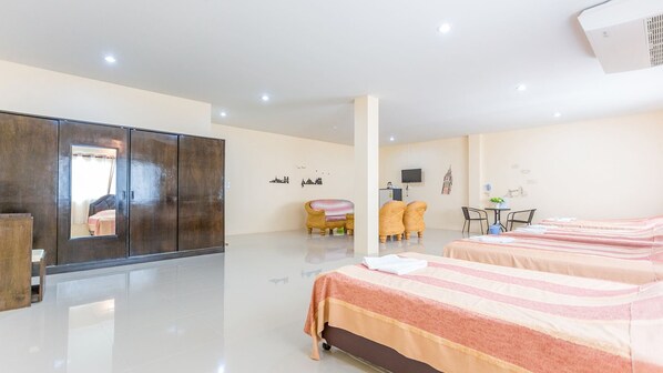 Habitación de hotel con un armario grande, dos camas, un área de estar con sofá y sillones, una mesita y un televisor.