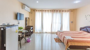 A hotel room with a bed, a desk with a chair, a refrigerator, and a television on the wall. - Phet Ngam Hotel (Mae Sai)