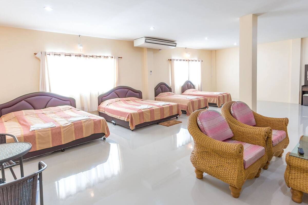 A hotel room with four beds, wicker furniture, a glass table, and a mirror.