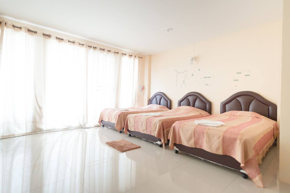 A hotel room with two beds, a large window with curtains, a map on the wall, and a polished floor.