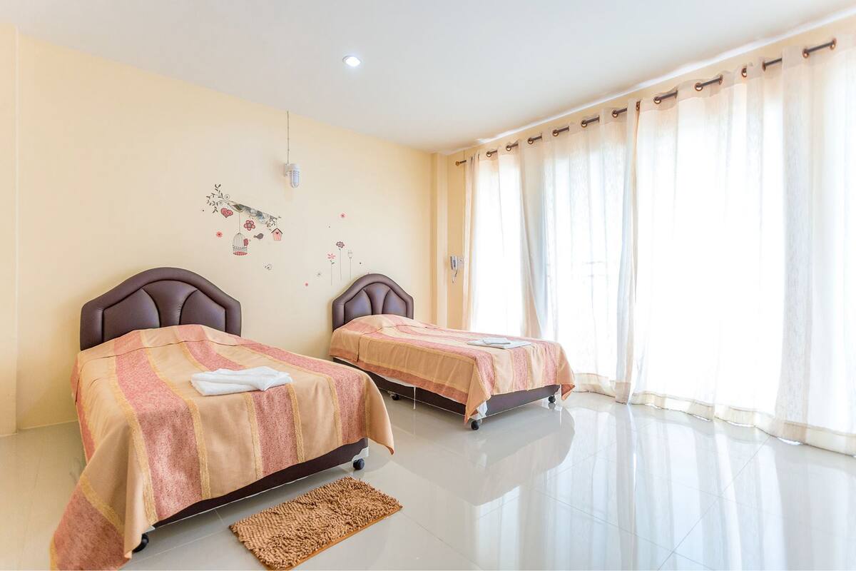 A hotel room with two beds, a large window with sheer curtains, and a decorative wall decal.