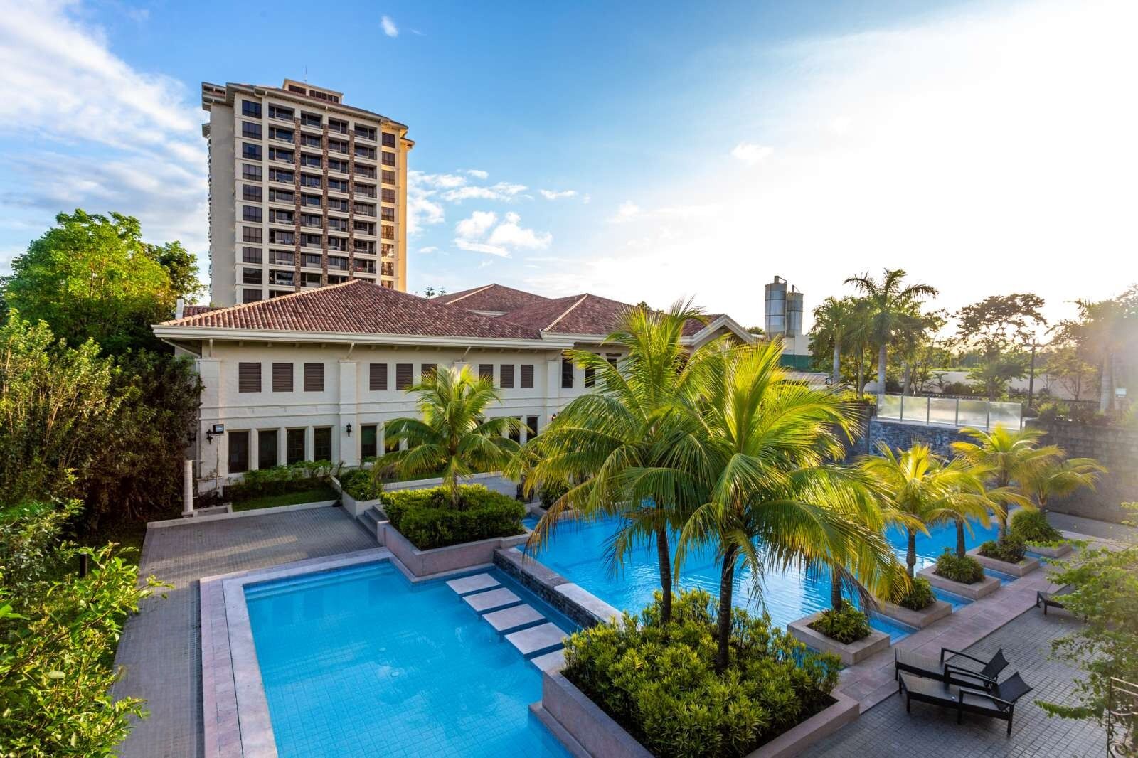 Un hotel con piscina, palmeras y un edificio grande al fondo.