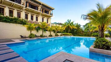A swimming pool with steps leading into it, surrounded by palm trees and a building with balconies.