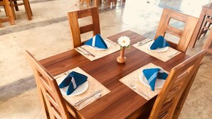 Una mesa de comedor de madera con servilletas azules, un plato blanco y un pequeño jarrón con una flor blanca.