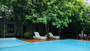 Una piscina con dos sillas reclinables blancas y una pequeña mesa.