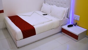 Cama bem arrumada com detalhe vermelho, cabeceira branca e mesa de cabeceira com telefone e carregador.