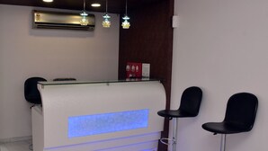 Uma área de recepção com um balcão de vidro, dois taboretes pretos e um painel iluminado em azul.