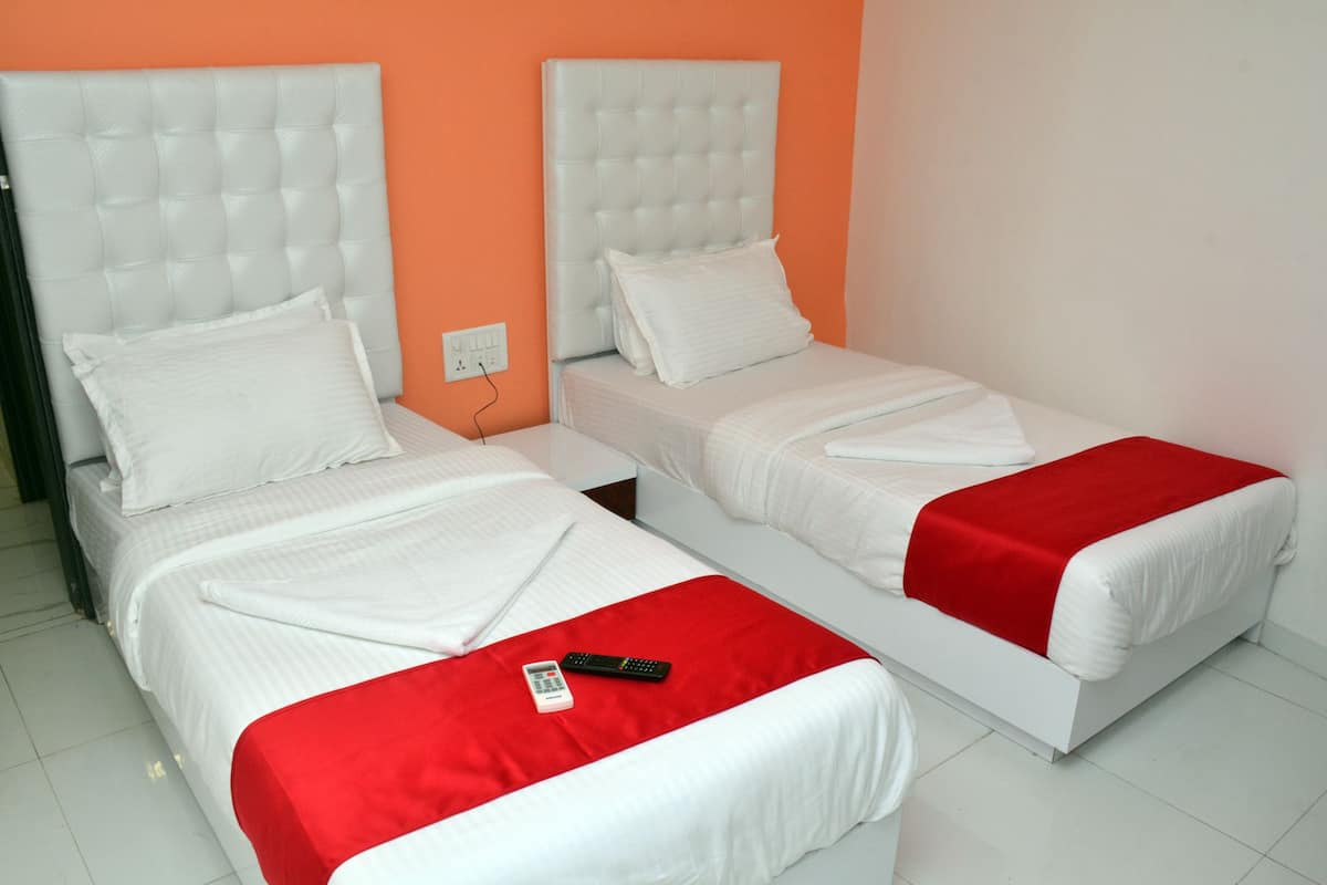 Quarto de hotel com duas camas, cada uma com roupa de cama branca e mantas vermelhas. Há um controle remoto na cama.