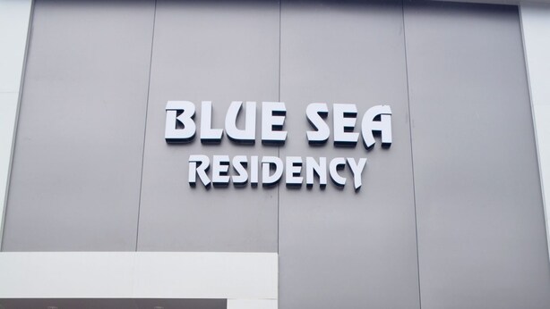 Exterior do Blue Sea Residency com design moderno, destacando uma placa e uma entrada de vidro.