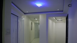 Um corredor com paredes brancas, piso de mármore e iluminação embutida.