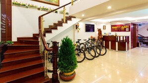 Vestíbulo de hotel con escalera, mostrador de recepción y bicicletas.