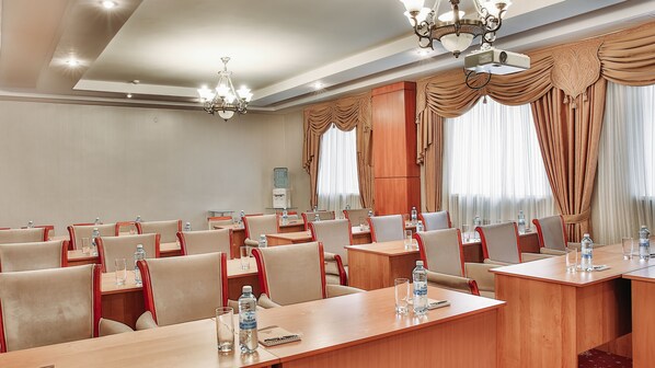 Un salón de conferencias con varias mesas y sillas, botellas de agua y una máquina de café.
