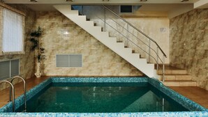 A swimming pool with a tiled edge, a staircase with metal railings, and a wall with a marble-like texture.