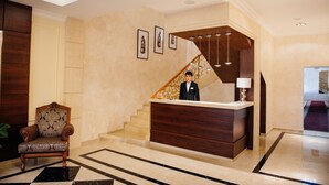 A hotel reception area with a wooden reception desk, a chair, and a staircase.