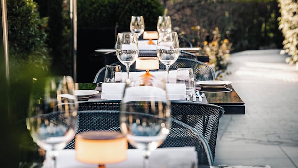 An outdoor dining area with tables set for a meal, surrounded by greenery. - Hôtel b design & Spa (Paradou)