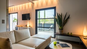 A modern hotel room with a sofa, a small table, a TV, a large window, and a potted plant. - Hôtel b design & Spa (Paradou)