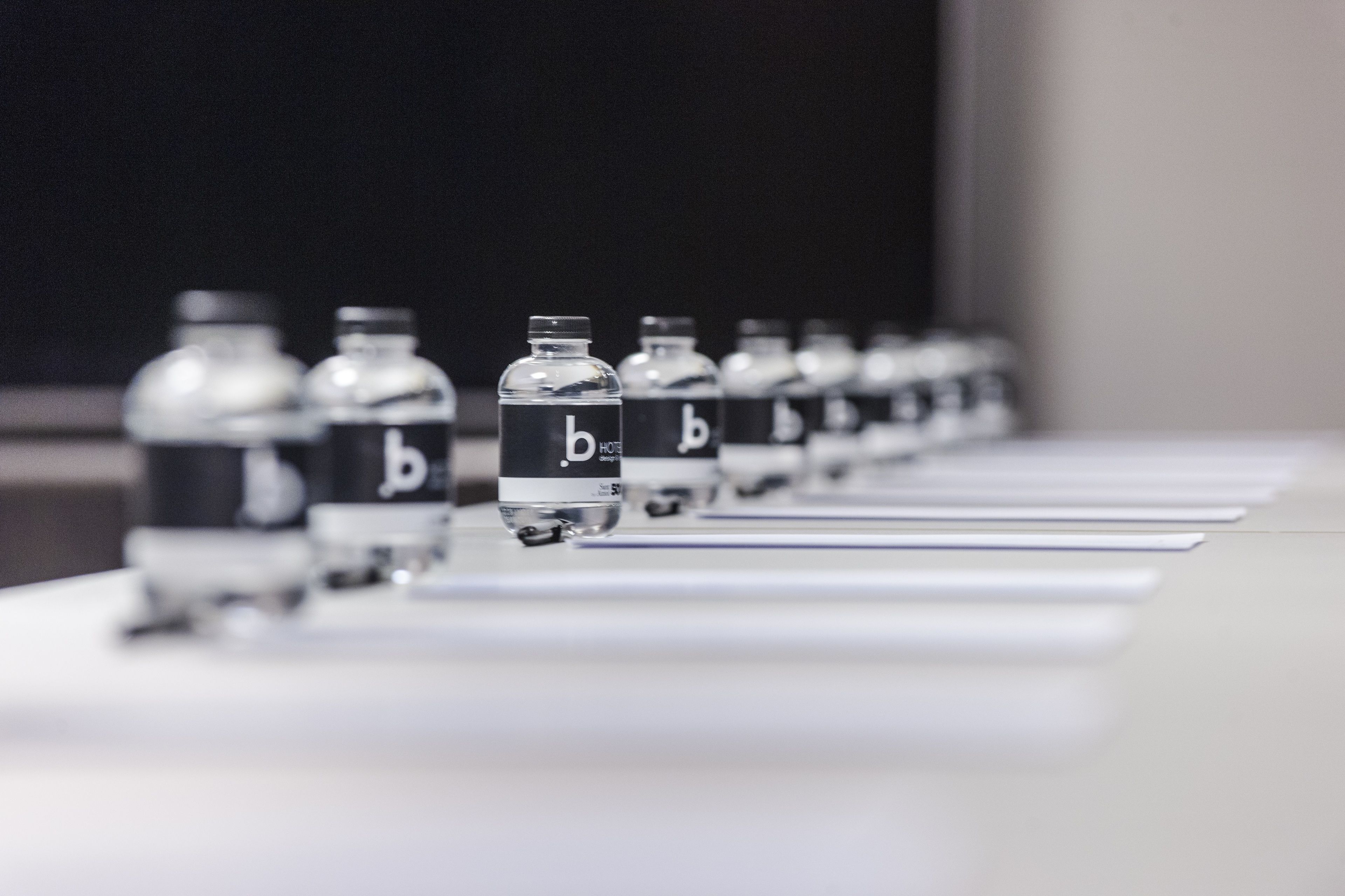 Une rangée de bouteilles identiques, toutes munies d’une étiquette, est posée sur une table.