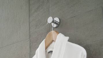 A white robe with a small logo hanging on a wooden hanger against a tiled wall.