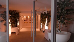A modern hotel lobby with a glass door, potted plants, and a reception desk. - Hôtel b design & Spa (Paradou)