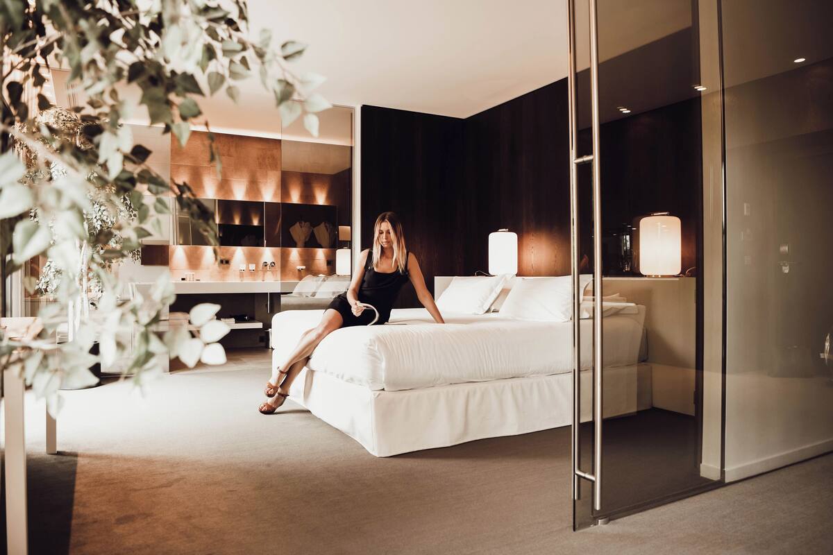 A modern hotel room with a large bed, a desk, and a glass partition.