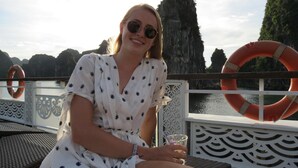 A person seated on a deck with a railing, overlooking a body of water and rocky cliffs. - Ngoc Anh Legend Hotel (Ninh Binh)