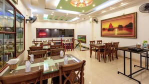 A restaurant with multiple dining tables and chairs, a ceiling fan, and a large framed painting on the wall. - Ngoc Anh Legend Hotel (Ninh Binh)