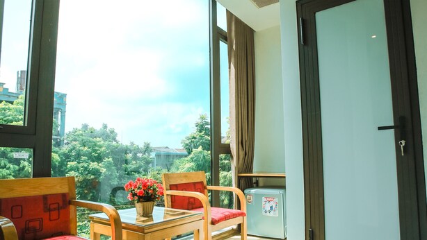 A room with large windows, a wooden table with chairs, a refrigerator, and a door with a mat. - Ngoc Anh Legend Hotel (Ninh Binh)